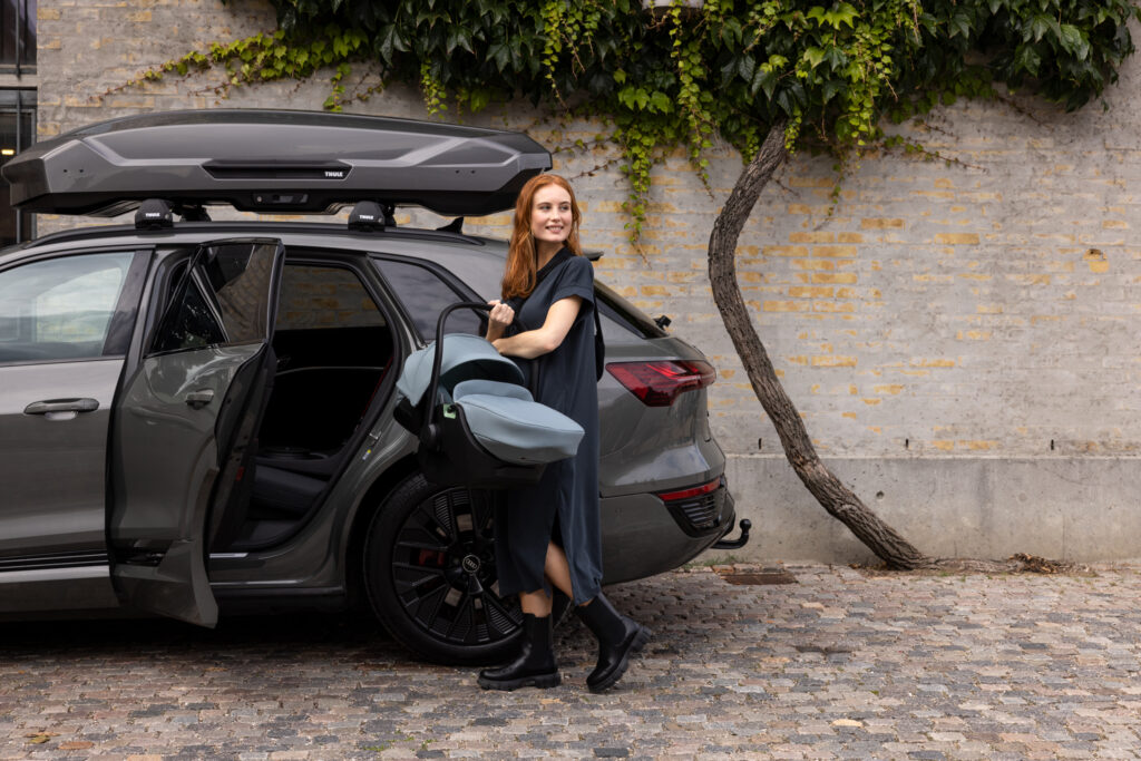 Frau steht vor einem Auto und hat einen Thule Kinder-Autositz im Arm