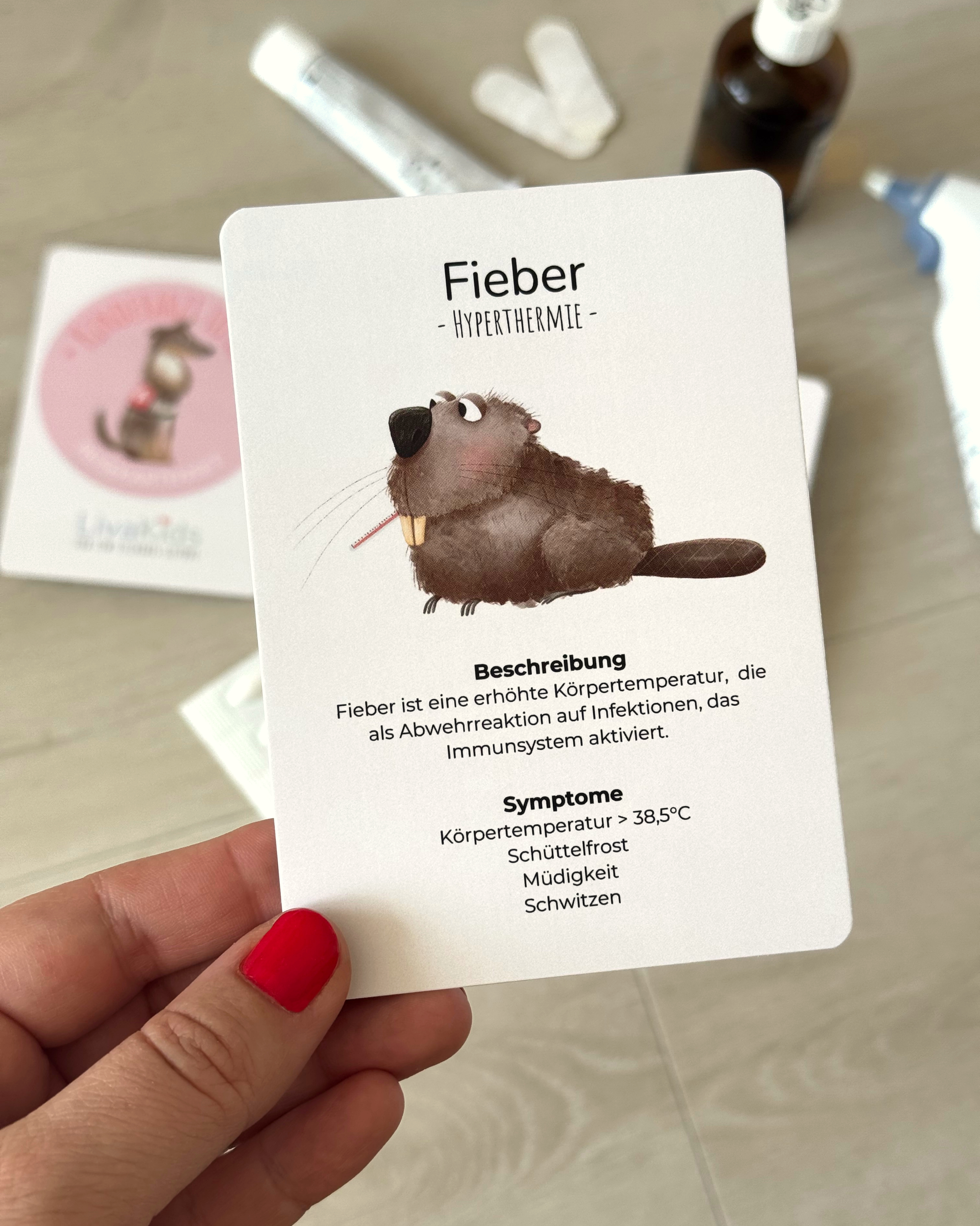 Eine Karte aus dem Kartenspiel LivaKids mit der Erläuterung zu Fieber bei Kindern, wird hochgehalten