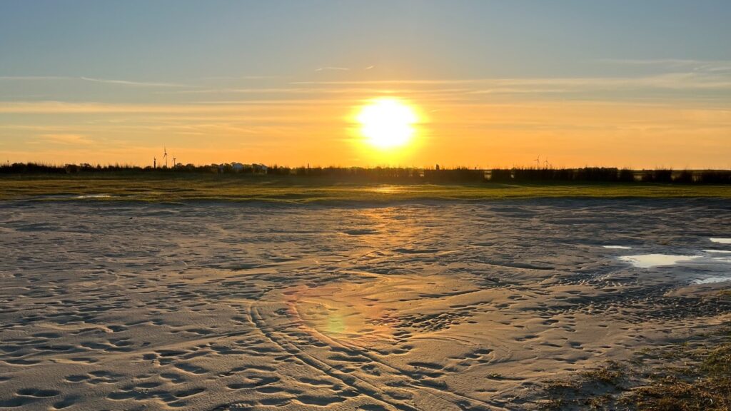 Sonnenuntergang über dem Watt an der Nordsee bei Dornum mit warmem Licht, ruhigem Himmel und spiegelnden Wasserflächen im Sand.
