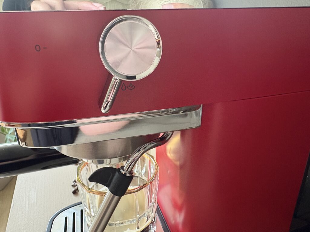 Detailaufnahme der roten Tchibo Lapressa Siebträgermaschine mit Dampflanze. Ein Glas steht unter der Dampfdüse auf der Abtropfschale, während der seitliche Drehregler zur Aktivierung der Dampffunktion gut sichtbar ist.